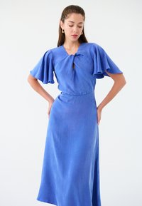 Niebieska lniana sukienka z krótkimi, zwiewnymi rękawami oraz wiązaniem przy dekolcie. Gładka faktura i dopasowany krój.