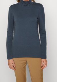 Mörkblå polotröja med lång ärm i ett mjukt tyg, med en åtsittande design och hög krage, kombinerad med ljusbruna byxor.