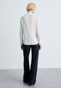 Hvid langærmet bluse med krave, kombineret med mørke højtaljede flared jeans. Glat stof med subtil struktur. Ingen synlige mønstre eller accenter.