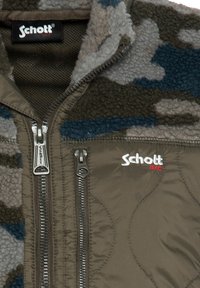 Kurtka polarowa w wzór camouflage z zamkiem błyskawicznym, w odcieniach oliwkowej zieleni, szarości i niebieskiego. Logo Schott w białym i czerwonym haftowanym napisie.