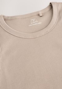 Débardeur beige côtelé avec un col rond et une coupe ajustée. Présente un tissu texturé et une petite étiquette indiquant l'origine.