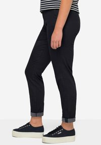 Pantaloni neri slim fit con risvolti, realizzati in un tessuto testurizzato. Abbinati a sneaker blu con lacci e suola bianca spessa.