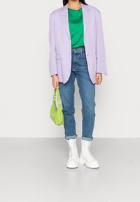 Blazer oversize lilas, haut en satin vert, jean taille haute bleu, bottes blanches épaisses, tenant un petit sac vert citron. Texture lisse partout.