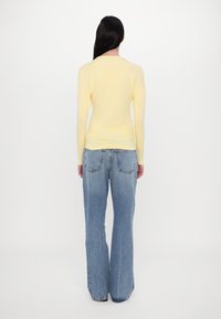Langärmliges, hellgelbes Oberteil mit taillierter Passform, kombiniert mit hochtaillierten, locker sitzenden hellblauen Jeans mit geflecktem Textur.