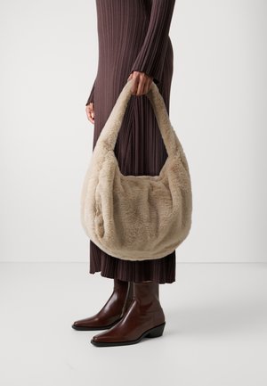 Person in a ribbed brown dress and brown leather boots holding a large beige faux fur handbag with a wide strap.