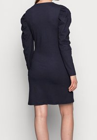 Marinblå långärmad klänning med strukturerad väv, figursydd silhuett och puffade axlar, med rundad halsringning och knälång fåll.