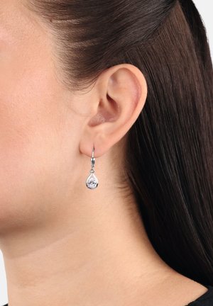 Orecchini a goccia in tonalità argento con pietra preziosa trasparente e sfaccettata, caratterizzati da un semplice design ad archetto e sottili decorazioni.