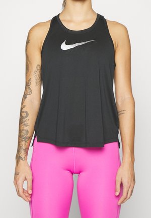 Frau trägt ein schwarzes ärmelloses Nike Tanktop und knallpinke Leggings, mit sichtbaren Tätowierungen am linken Arm und die Hände entspannt an den Seiten.