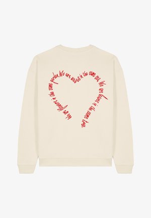 Krém színű pulóver, piros szív alakú grafikával a hátsó részén, kézzel írt szöveggel. Puha anyag, bordázott mandzsettákkal és szegéllyel.