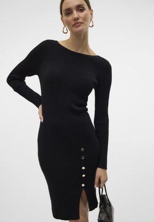 Juodasis, grublėtas megztinis su ilgais rankovėmis, bepečių iškirpte, šoniniu įpjovimu ir penkiais auksiniais mygtukais palei apačią.