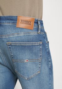 Jeans in denim blu con etichetta in pelle Tommy Jeans in vita, caratterizzati da un'etichetta logo rosso-bianco-blu sulla tasca posteriore.