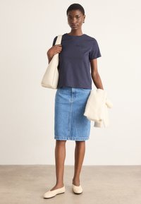 Tricou din bumbac bleumarin cu logo, fustă tip creion din denim bleu deschis, geantă crem și balerini de culoare deschisă, având o textură netedă.