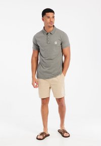Grijze polo met een knoopsluiting, gecombineerd met beige gestreepte shorts. Beide artikelen hebben een klein logo-embleem. Draag met bruine sandalen.