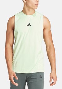 Top atletico senza maniche di colore verde chiaro con scollatura rotonda, caratterizzato da un piccolo logo Adidas nero sul petto e un design aerodinamico.