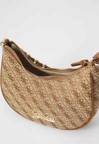 Sac à main en tissu marron avec un motif monogramme, fermeture éclair dorée et accent de logo. Présente une forme incurvée et une surface texturée.