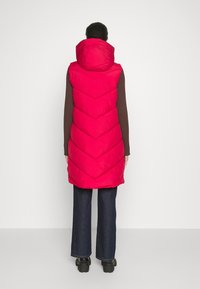 Felle roze gewatteerde vest met capuchon, met een chevronpatroon. De achterkant is glad en is gecombineerd met een bruine lange mouwen shirt en donkere flared jeans.