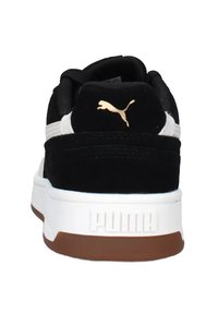 Zapatillas negras de ante con detalles blancos, que presentan un logo dorado de Puma en el talón y una suela de goma con detalles en marrón.