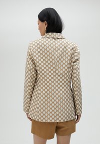 Mönstrad kavaj med en krämfärgad bas och ett geometriskt mönster i beige, med strukturerad passform, snedställda slag och utan knapplåsning.