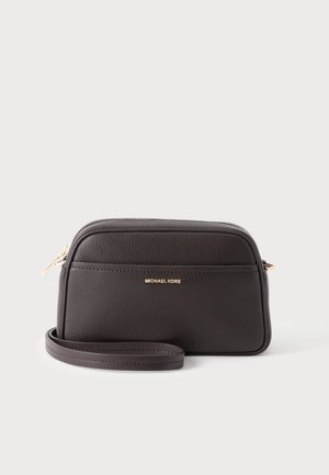 Lille sort Michael Kors crossbody-taske i læder med guldfarvet lynlås og logo, placeret mod en ensfarvet lys baggrund.