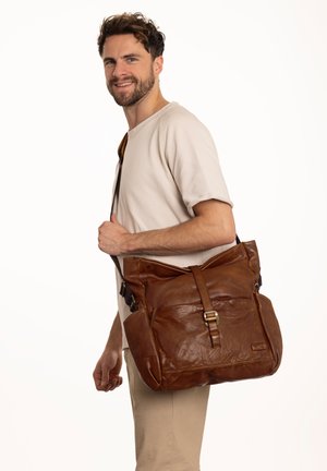 Borsa a tracolla in pelle marrone con finitura testurizzata, tracolla regolabile e dettaglio con fibbia anteriore, indossata da un uomo su uno sfondo bianco.