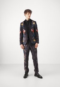 Black patterned suit with colorful butterfly motifs, featuring a tailored blazer and slim-fit trousers, paired with a black shirt and shoes.