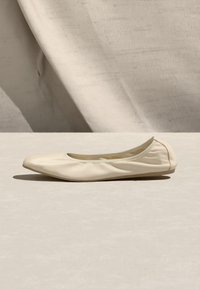 Μπαλαρίνα από απαλό δέρμα σε κρεμ χρώμα με στρογγυλή μύτη, τοποθετημένη σε φωτεινή επιφάνεια με ουδέτερο υφασμάτινο φόντο.