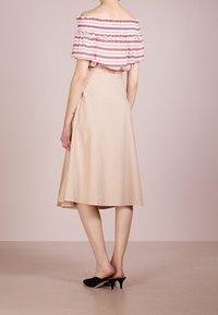 Top sin mangas con rayas rojas, combinado con una falda beige a la altura de la rodilla. La modelo lleva unas mules negras de tacón, mostrando una textura de tela suave.