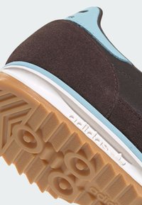 Brown suede sneaker with light blue accents, featuring a textured rubber sole and white midsole, angled view highlighting the design.