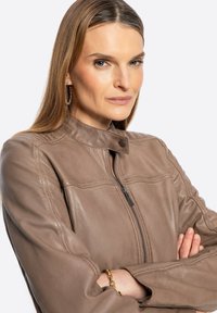 Braune Lederjacke mit hohem Kragen, Reißverschluss und kontrastierenden Nähten. Glatte Textur und taillierte Passform mit sichtbaren Nähten.