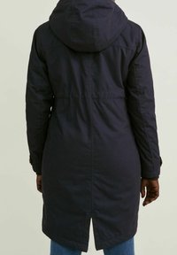 Parka azul marino con capucha, diseño de longitud media, textura suave, cintura con cordón y detalle de abertura en la parte posterior. Mangas largas con detalles de botones.