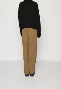 Suéter negro de punto con un corte holgado, combinado con pantalones cargo color beige que tienen bolsillos laterales y están hechos de una tela ligera y suave. Botas negras.