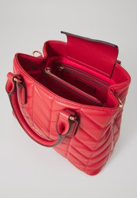 Röd quiltad handväska i läder med dubbla handtag, guldtonad hårdvara och ett inre med flera fack och en blixtlåsficka.