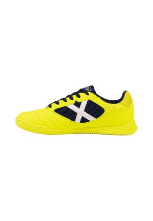 Zapatilla deportiva de color amarillo brillante y negro con detalle blanco en forma de cruz, diseño con cordones y suela texturizada vista de lado.