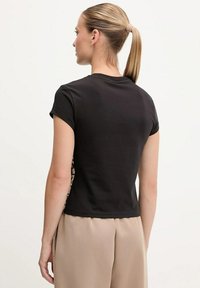 T-shirt nera a maniche corte con un design aderente e una schiena texturizzata. La parte anteriore presenta una finitura liscia e un collo rotondo.