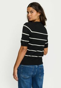 Črna kratka majica s kratkimi rokavi z belimi vodoravnimi črtami, rebrastim ovratnikom in oprijetim robom. Kombinirana z modrimi džins hlačami.