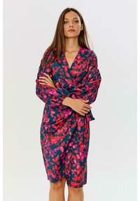 Květinové šaty do tvaru zabalí s tmavě námořnickým pozadím a živými růžovými a červenými listovými vzory. Dlouhé rukávy s nařasenými manžetami, délka ke kolenům.