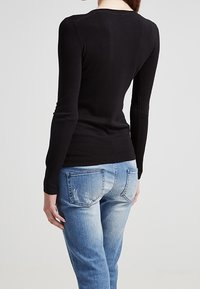 Černý svetr s dlouhým rukávem, ribbovanou strukturou, přiléhavý střih a zakulacený výstřih, v kombinaci se světlými modrými džíny s kapsami vzadu.