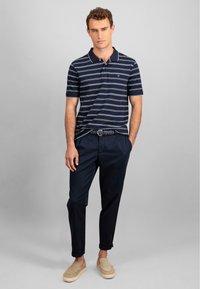 Polo tričko s krátkým rukávem pruhované v námořnickém stylu, spárované s tmavými kalhotami a béžovými slip-on botami. Obsahuje texturovaný pletený opasek.