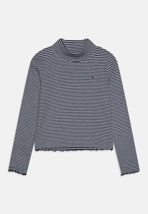 Czarny i biały golf w poziome paski z długim rękawem, z małym haftowanym logo na piersi i falbankami na krawędziach.