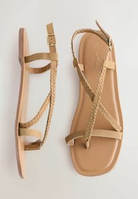 Tannfarvede flade sandaler med flettede stropper, justerbar spænde og glat sål. Overdelen kombinerer flade og flettede elementer.