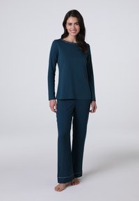 Maglietta verde acqua a maniche lunghe con scollatura rotonda e cuciture decorative abbinata a pantaloni larghi coordinati. Tessuto morbido. Modello a piedi nudi.