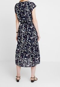 Marinblommig klänning med korta ärmar, sammanknuten midja och en flödande fåll. Flerfärgade blomstertryck täcker tyget, med en lätt textur.