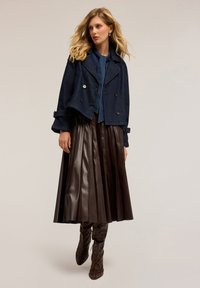 Chaqueta de mezclilla navy de doble botonadura sobre una blusa azul, combinada con una falda de piel marrón con pliegues y botas de caña alta con patrón.