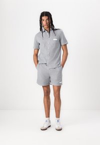 Stribet kortærmet skjorte og matchende shorts i grå og hvidt stof med en lomme og et lille logo-patch. Hvide sneakers fuldender looket.