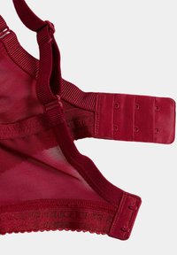 Roter BH-Träger und Rückenschluss mit drei Haken- und Ösenverschlüssen sowie verstellbarem Schultergurt vor weißem Hintergrund.