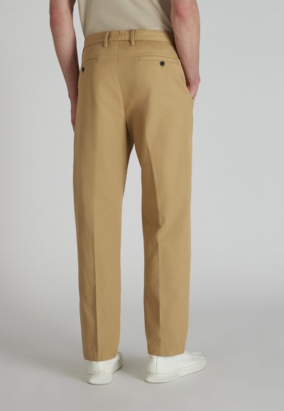 Khaki broek met een rechte snit, voorzien van twee achterzakken met zwarte knopen, gedragen met witte sneakers. Gladde stofstructuur.