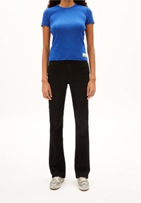 Sininen istuva lyhythihainen t-paita yhdistettynä mustiin liehukehousuihin. Teksturoitu kangas, jossa on pieni valkoinen etiketti paidan helmassa. Mustat ja valkoiset kengät.