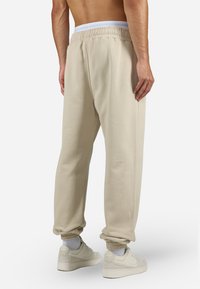 Beige joggebukser med elastisk liv, med en avslappet passform, oppbrettede anklene og en myk tekstur. Brukt med hvite sokker og sko.