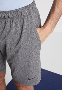 Pantalones cortos deportivos grises con una tela texturizada, cinturilla elástica y bolsillos laterales. Presenta un logo de Nike negro en la parte inferior izquierda.