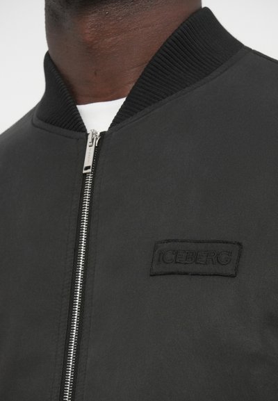 Μαύρο μπουφάν τύπου bomber με ριμπ γιακά, κλείσιμο με φερμουάρ και ανάγλυφο έμβλημα "ICEBERG" στο αριστερό μέρος του στήθους. Λείο υφασμάτινο υλικό.